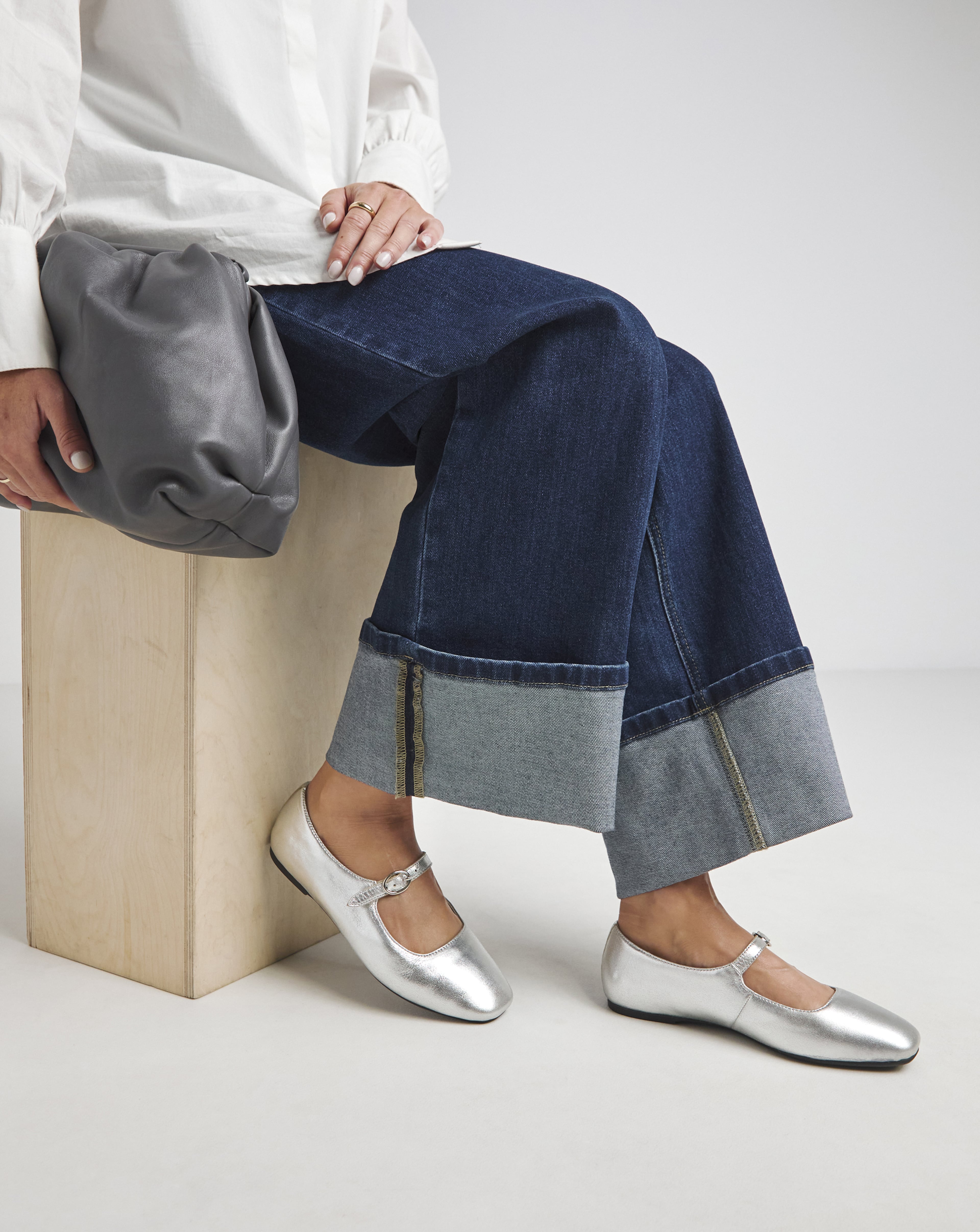 A woman sat wearing Loose fit jeans and silver flat sandals
