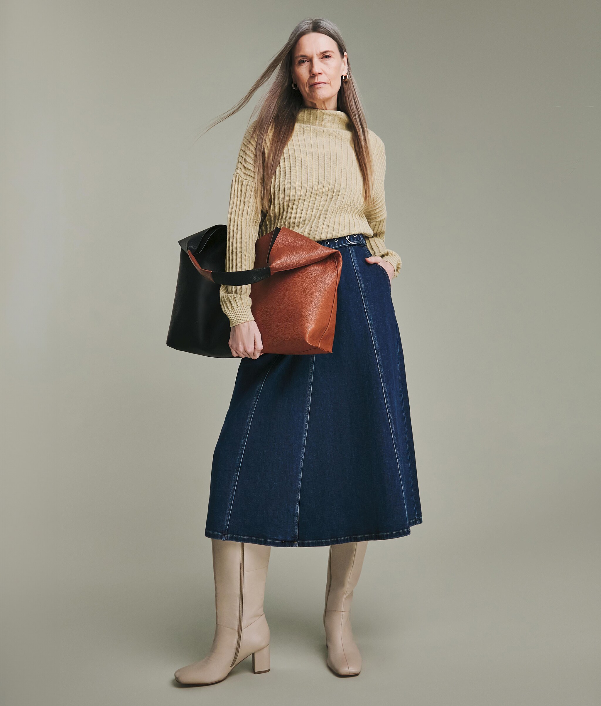 A woman stood wearing a taupe pullover, blue A line shirt and taupe leather boots